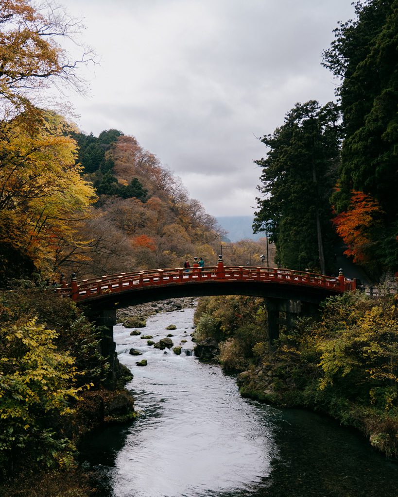 Red arched Shinkyo Bridge crossing the Daiya River surrounded by autumn foliage in Nikko