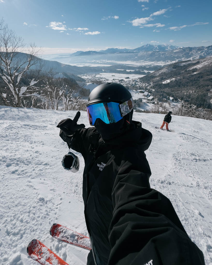 Skier taking a selfie overlooking Nozawa Onsen village and the surrounding valley on a clear day