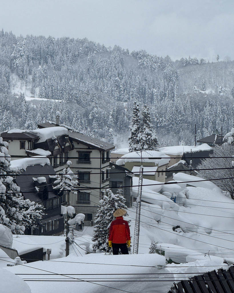 Person overlooking heavy snowfall on traditional rooftops in Nozawa Onsen village, Nagano
