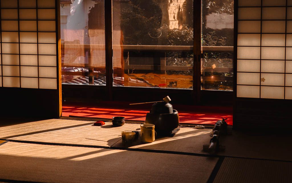 Traditional tea ceremony utensils laid out on a tatami mat in a sunlit room