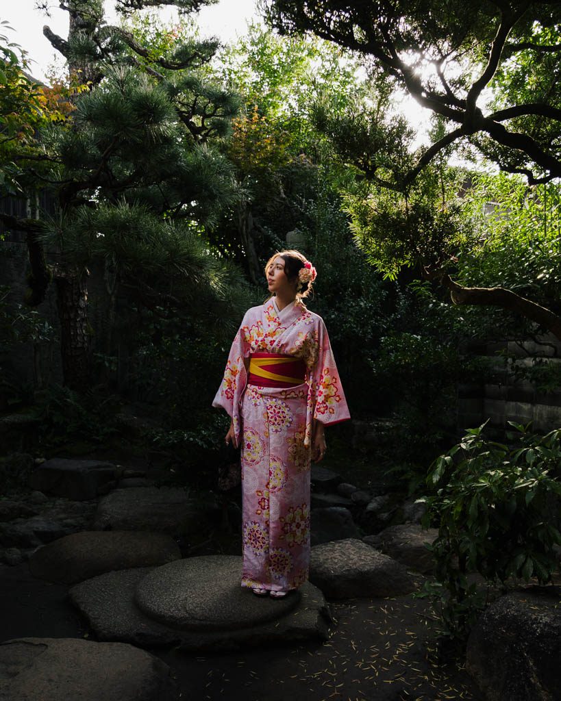 Woman in a pink floral kimono standing in a traditional Japanese garden