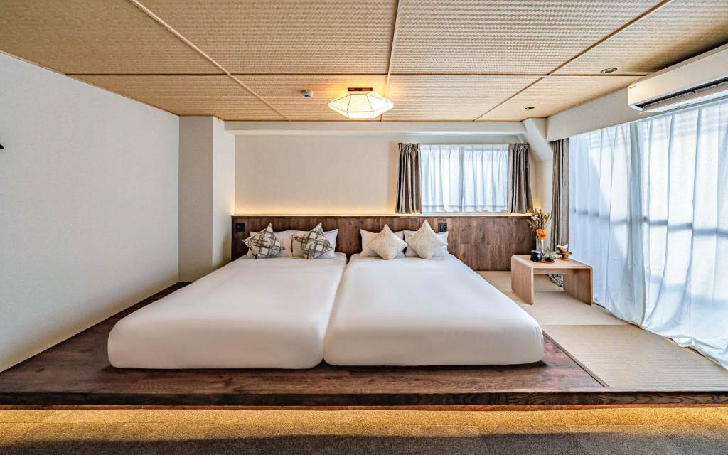 Japanese-style twin room with two beds on a raised wooden platform, tatami ceiling, and sheer curtains