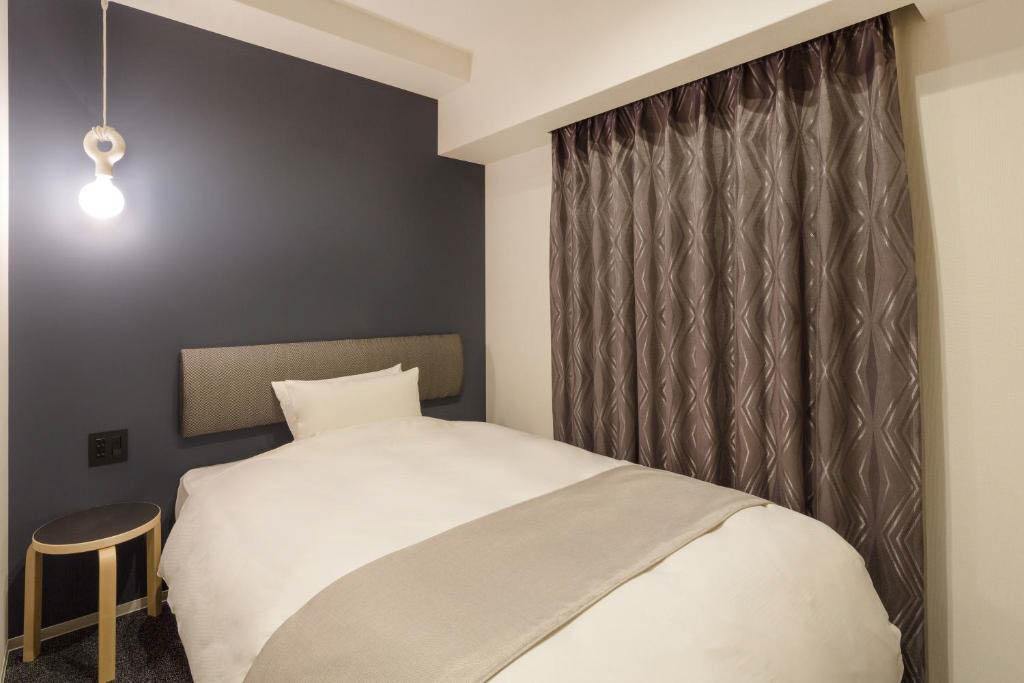 Compact hotel room with a double bed, upholstered headboard, pendant light, and patterned curtains