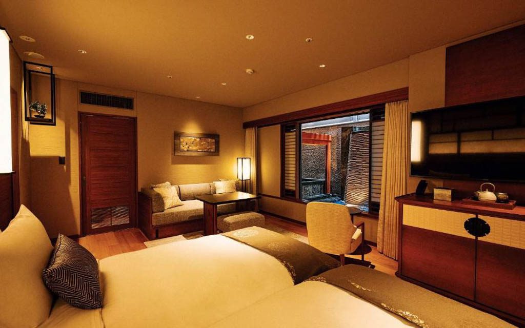 Hotel suite bedroom with a sofa seating area, large TV, and window overlooking a private balcony