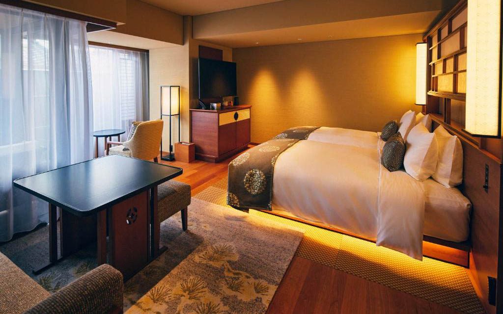 Hotel suite with a bed, dining table and chairs, armchair, and wall-mounted TV