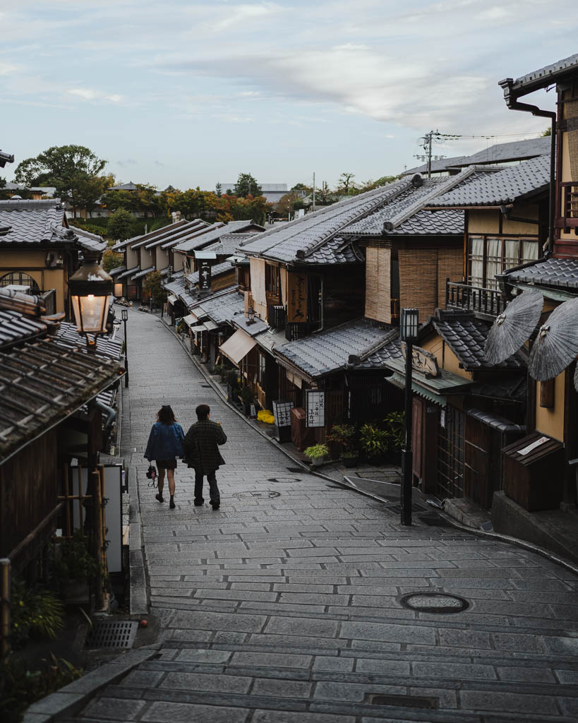 Couple walking down a stone-paved street lined with traditional wooden townhouses in Higashiyama, Kyoto