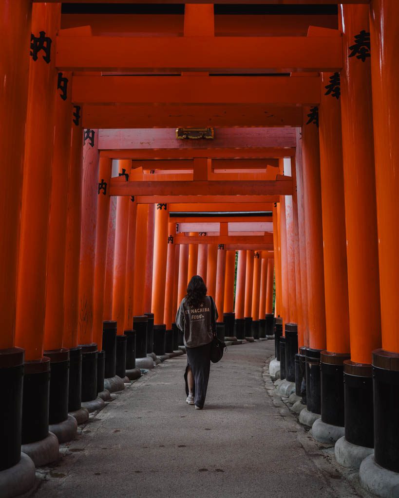 Woman walking along a path lined with orange torii gates at Fushimi Inari Shrine in Kyoto