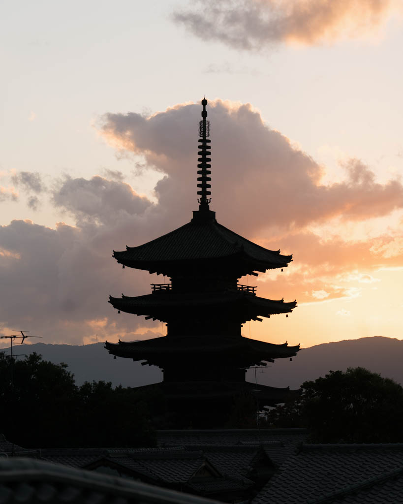 The silhouette of Yasaka Pagoda against an orange and pink sunset sky, with mountains and tiled rooftops in the distance